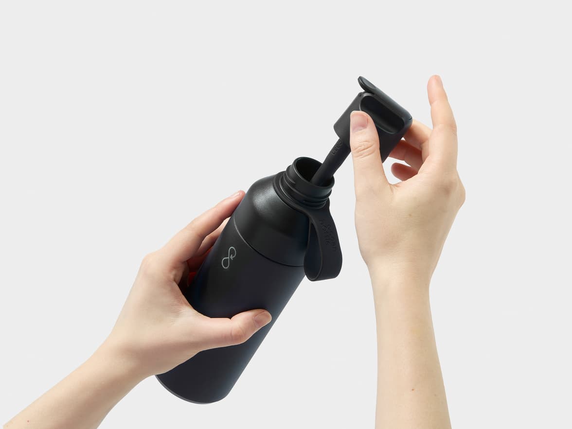 A black Ocean Bottle water bottle being opened by hands.