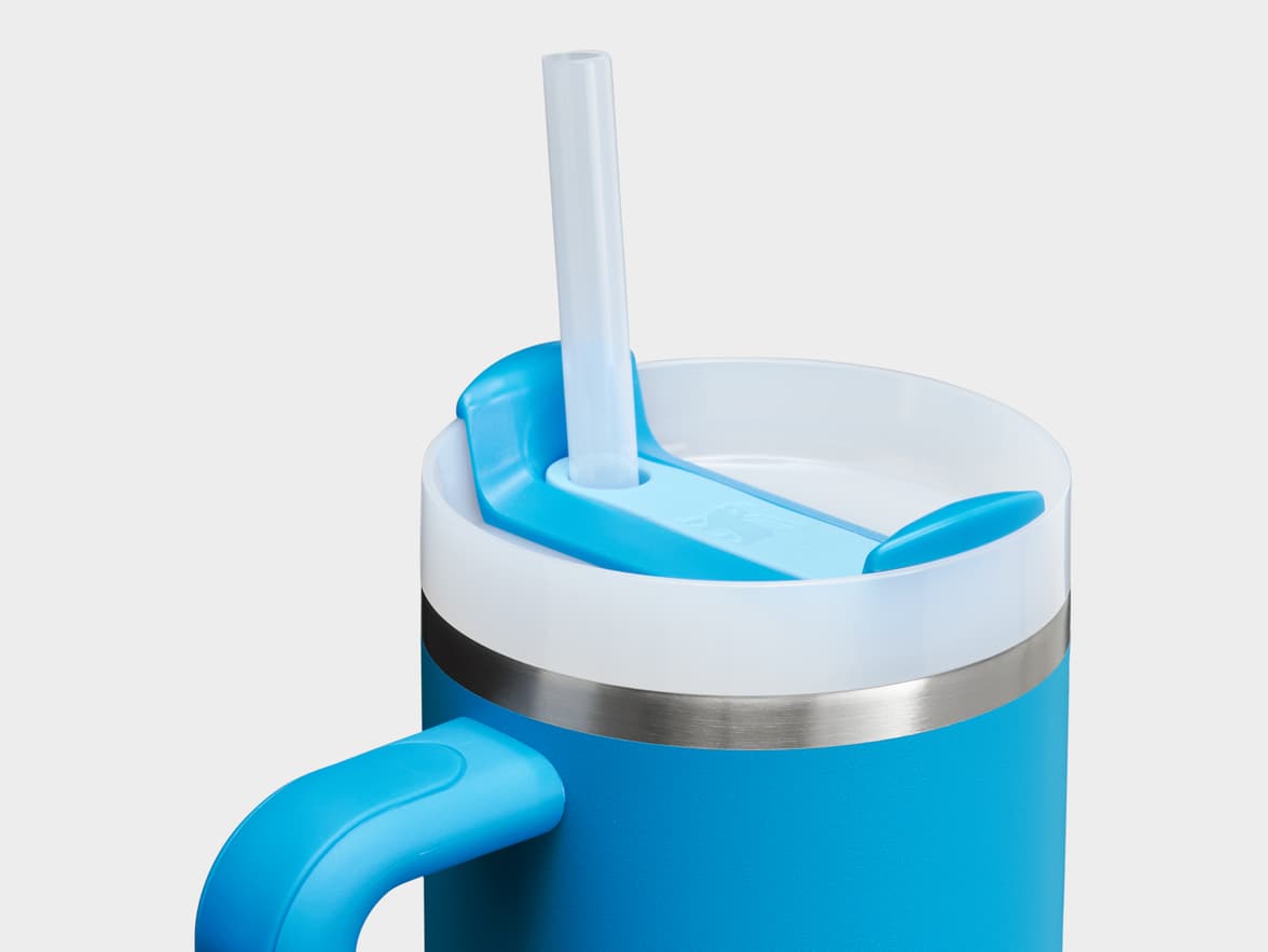 A blue travel mug with a white lid, a clear straw, and a blue handle.