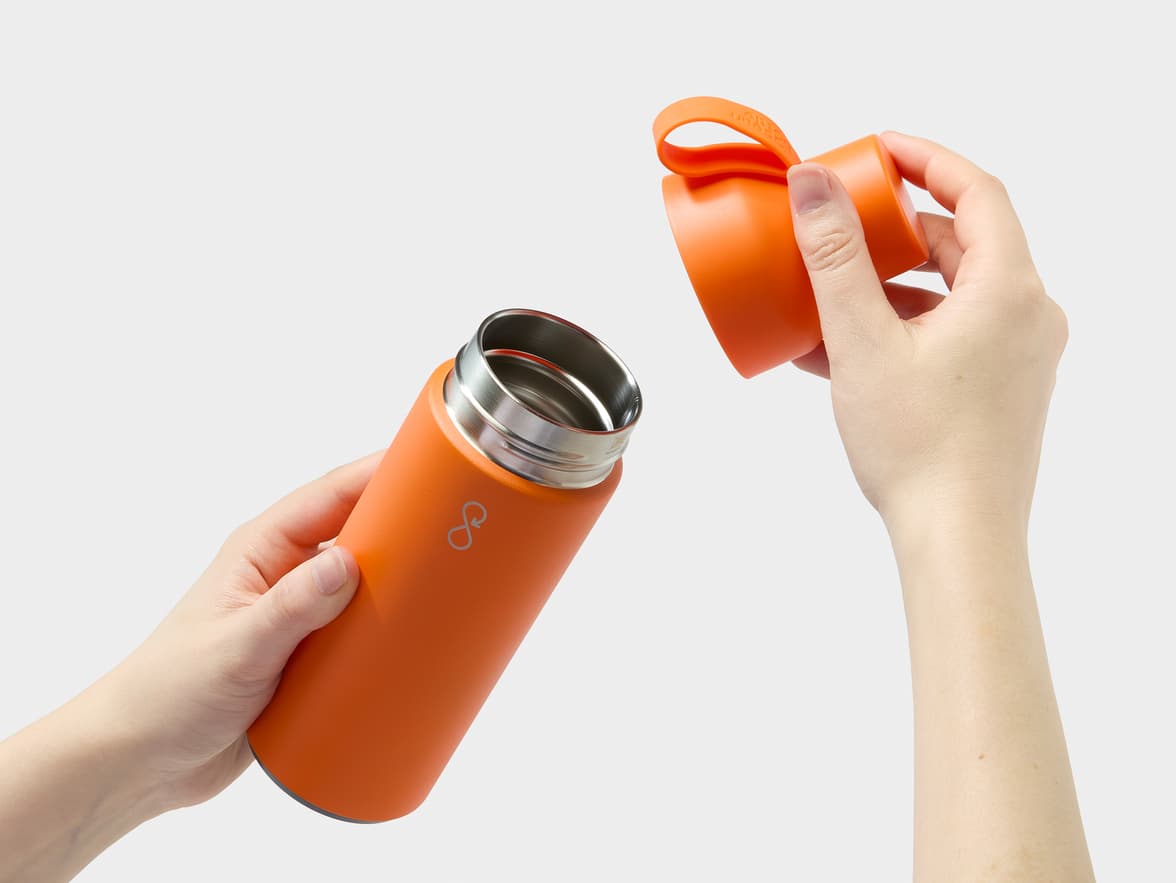 An orange 'A BIG OCEAN' water bottle is held open by hands.