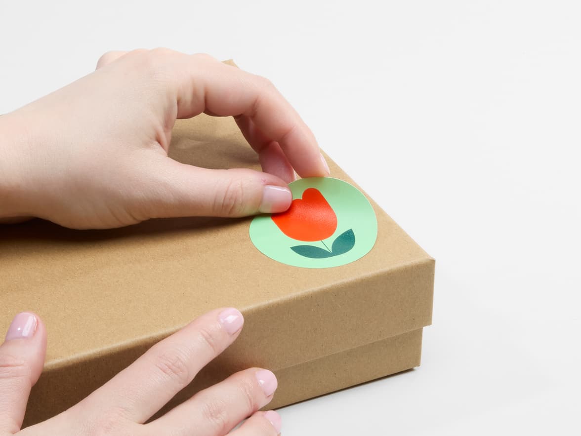 A person placing a customized matte paper sticker on a cardboard box.