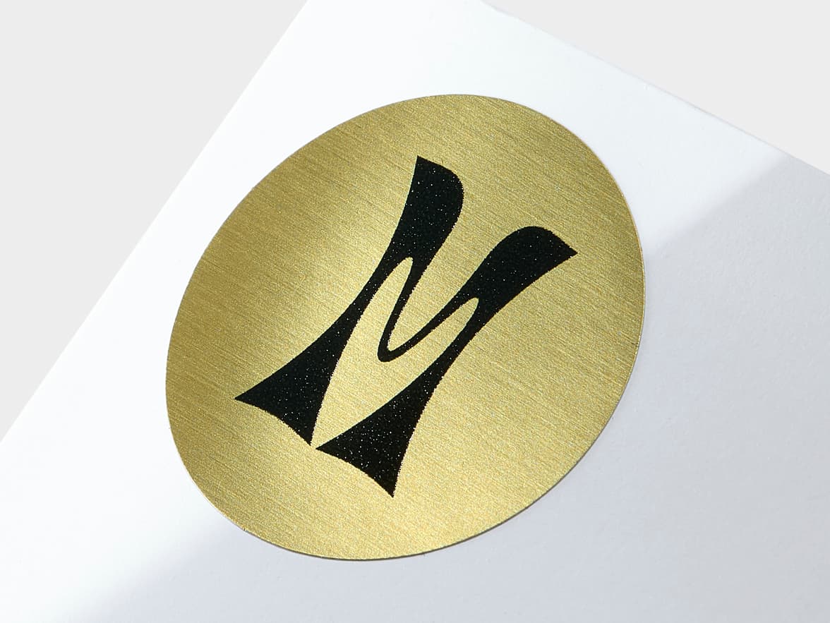 A close up image of a round gold metallic sticker with black customization.
