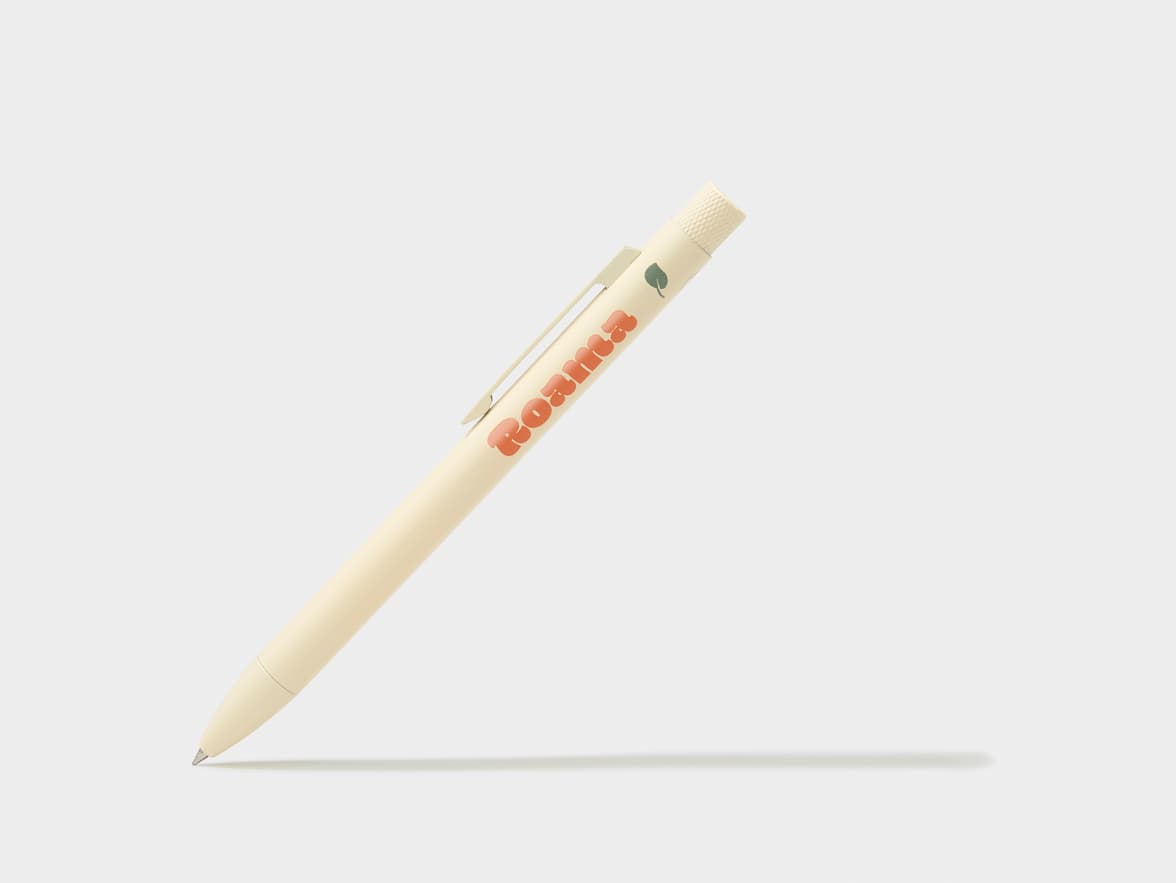 Cream-colored "Roama" pen with a green leaf logo, angled on a white surface.