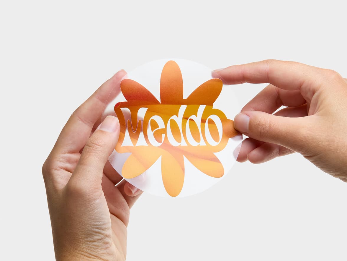 Hands holding a clear round sticker with a large orange flower printed on it.