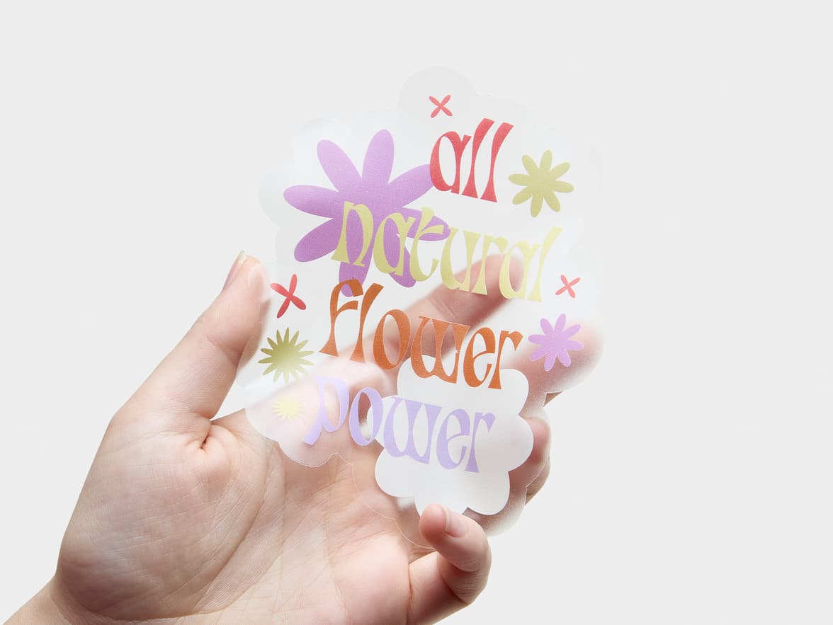 A hand holding a clear die cut sticker with flowers on it and the words 'all natural flower power'.