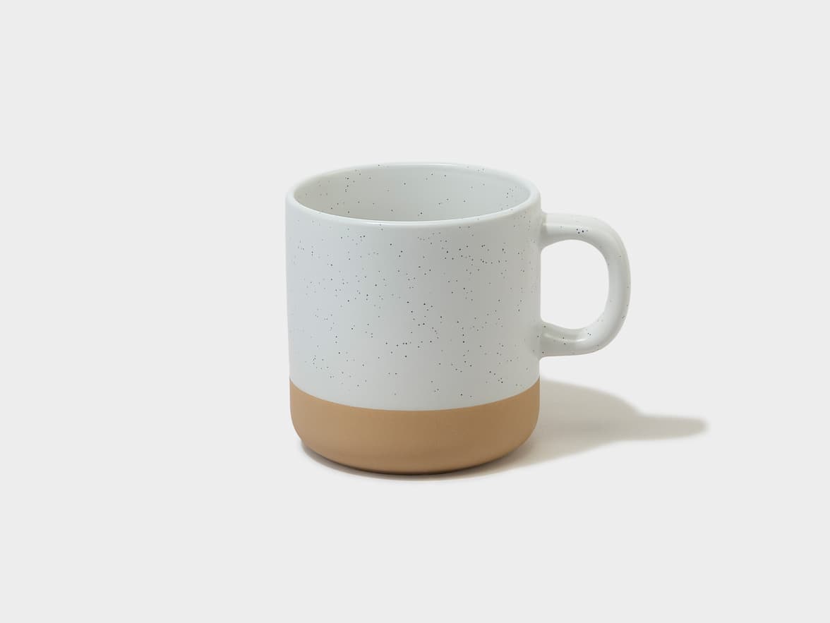 A speckled white ceramic mug with a tan base and handle.