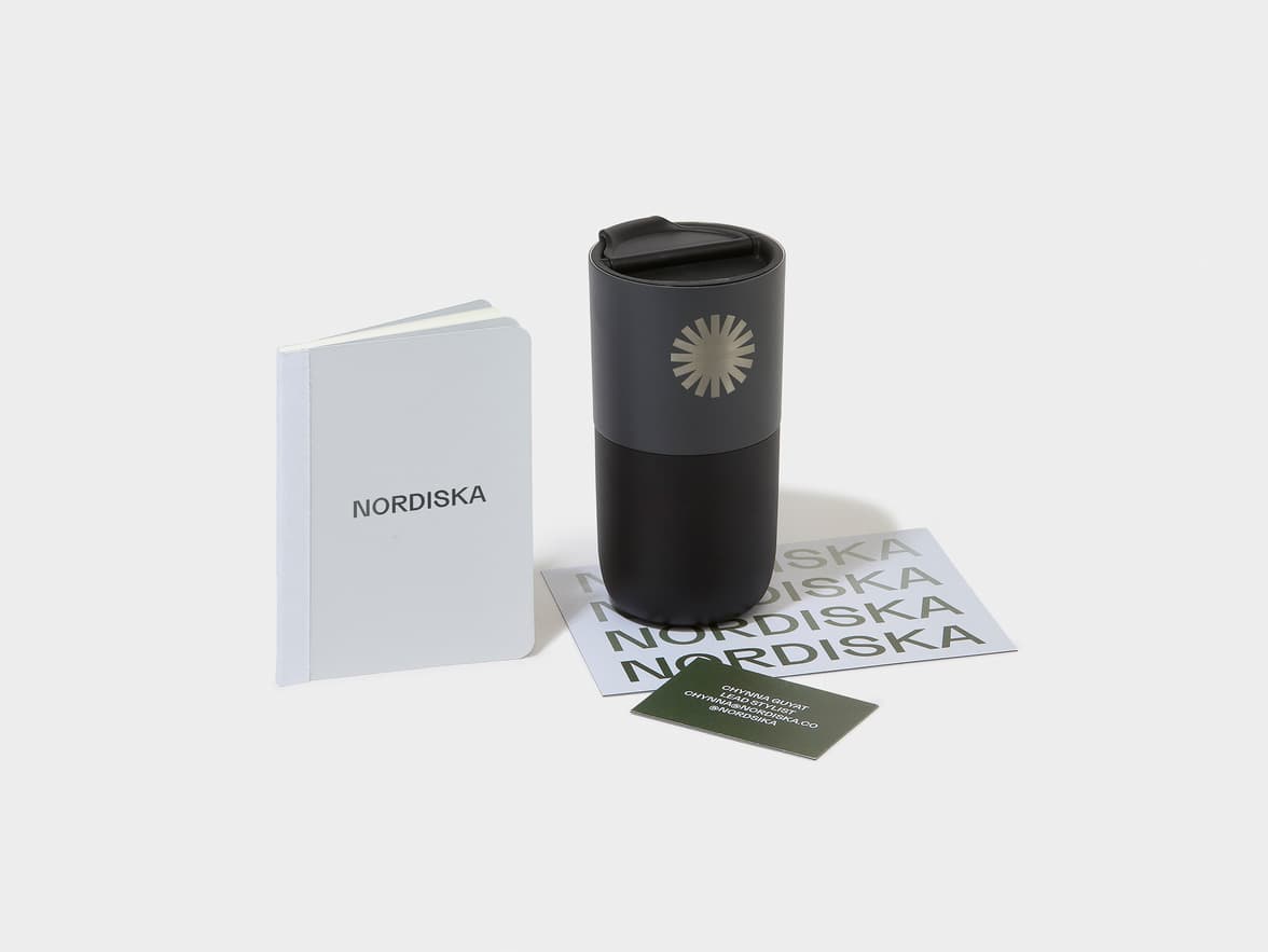 A dark grey and black NORDISKA tumbler with a sunburst logo.