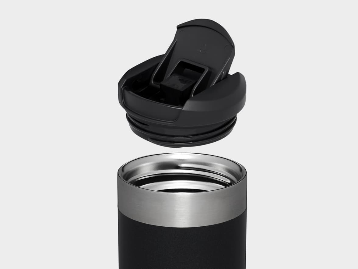Black travel mug with a silver band and its open black flip-top lid floating above it.