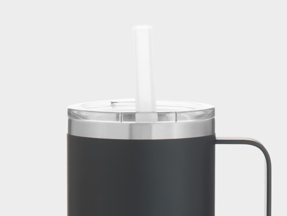 Close-up of a matte black travel mug with a clear lid and a white straw, featuring a silver band below the lid and a black handle visible on the right, against a plain light grey background.