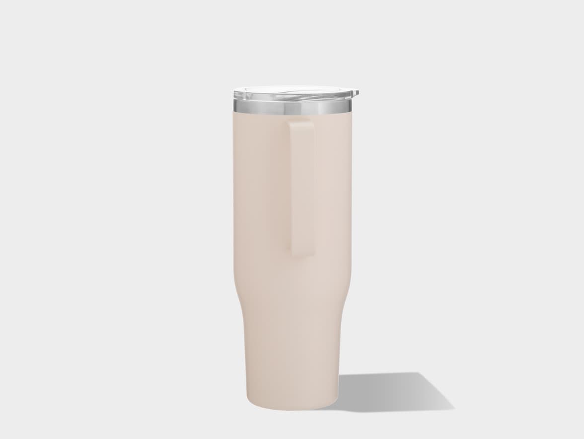 A tall, light beige or cream-colored insulated tumbler stands upright against a plain, light grey background. It has an integrated handle running down one side. The top features a clear, transparent lid with a silver-colored metallic band just below it. A soft shadow extends from the base of the tumbler to the right.