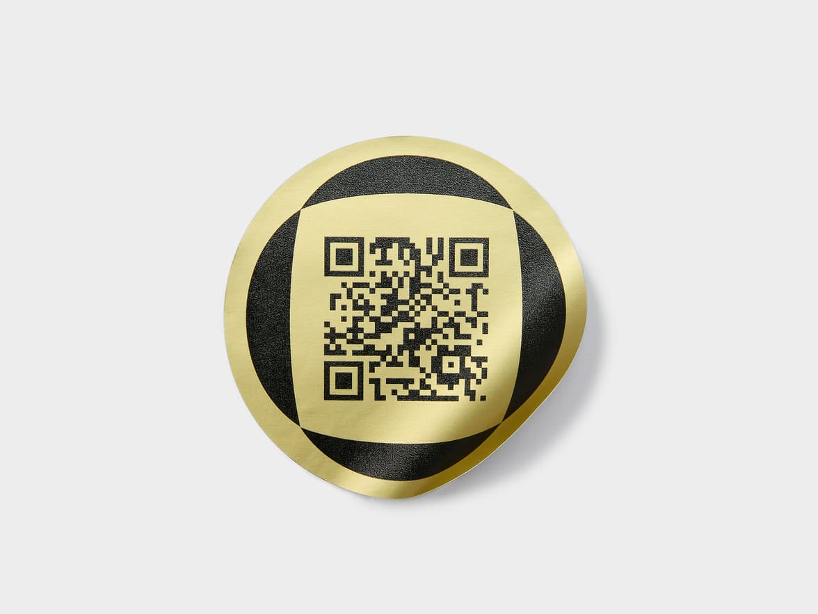 A round gold metallic sticker with a black QR code on it.