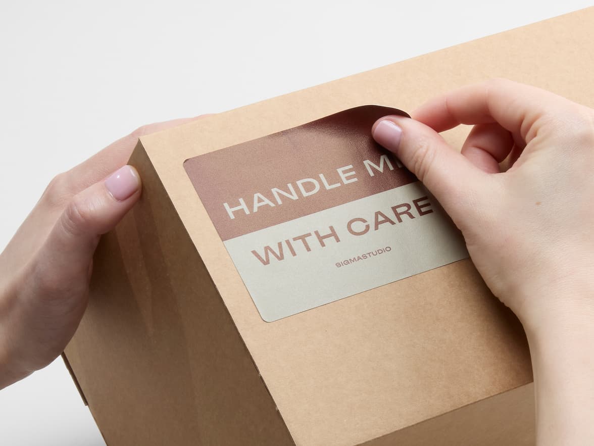 A person placing a customized matte paper sticker in size 4x3 on a cardboard box.