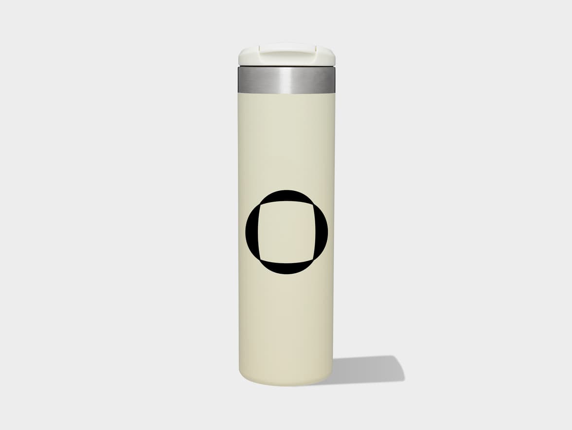 A cream-colored travel Stanley mug with a white lid, a silver band, and a black abstract circular and square logo.