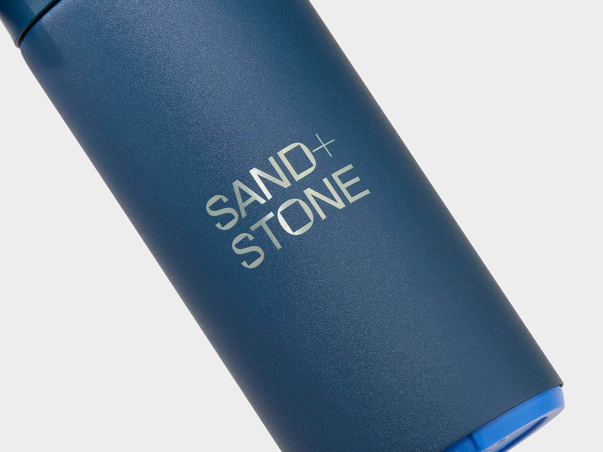 Dark blue textured bottle with "SAND+ STONE" logo.