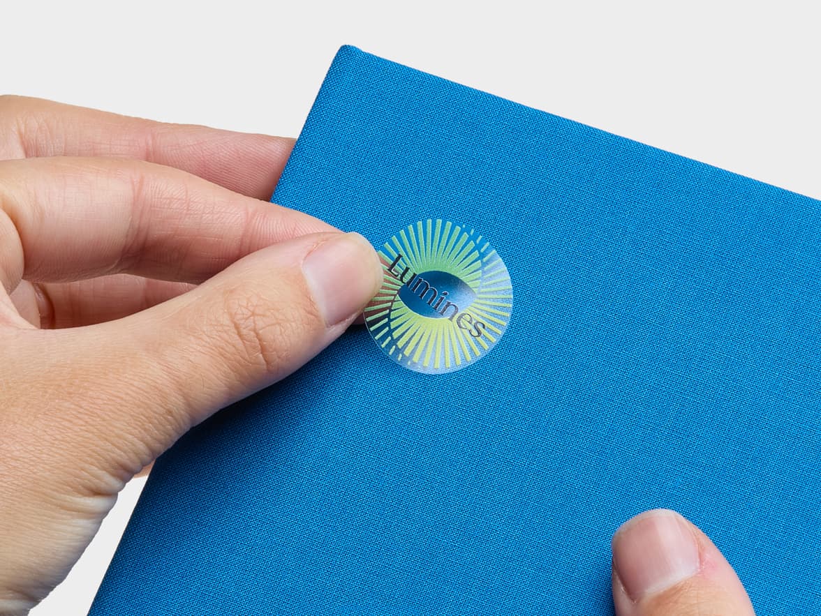 A hand placing a customized clear round sticker onto a blue box.