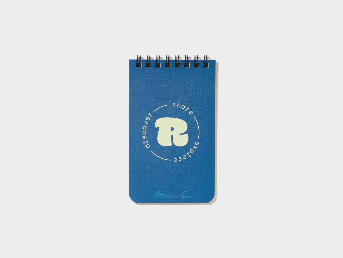 Blue spiral-bound notebook with "discover, share, explore" around a stylized "R" logo and "Rite in the Rain" text on the cover.