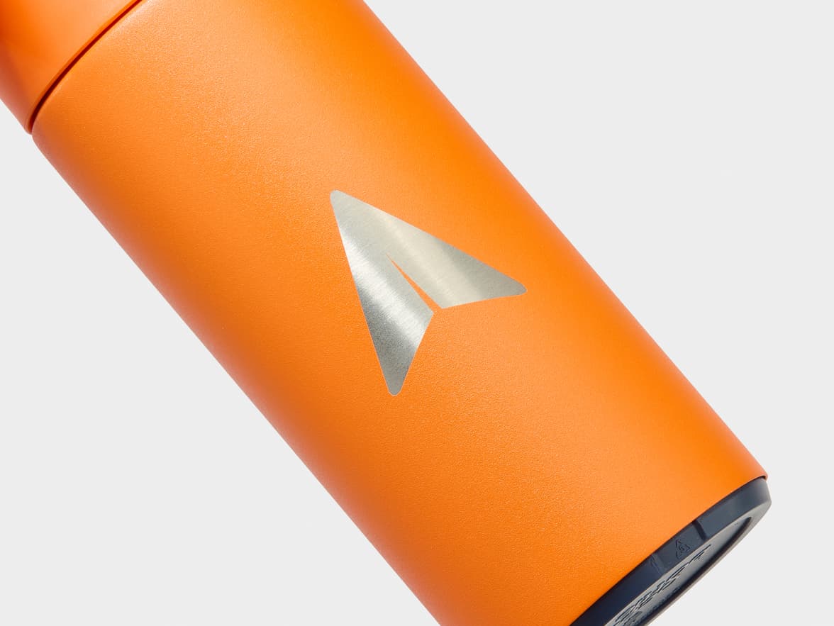 A textured orange bottle with a silver paper airplane logo.
