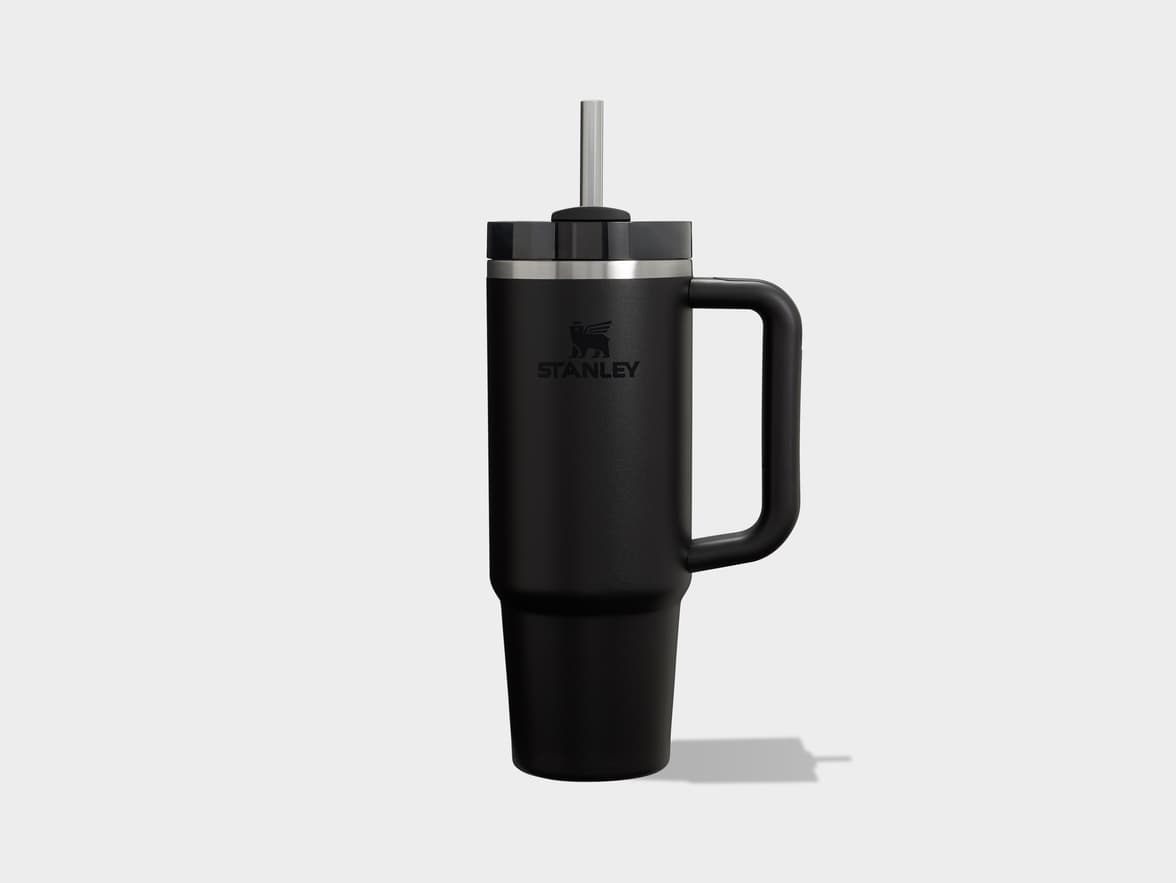 Black Stanley tumbler with a handle and straw on a light gray background.
