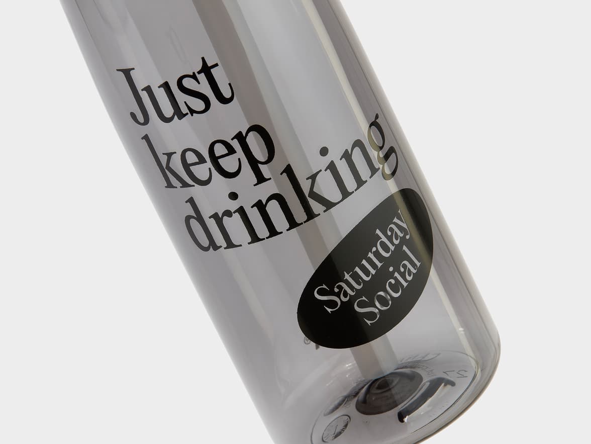 A transparent grey bottle with the text 'Just keep drinking' and 'Saturday Social' branding.