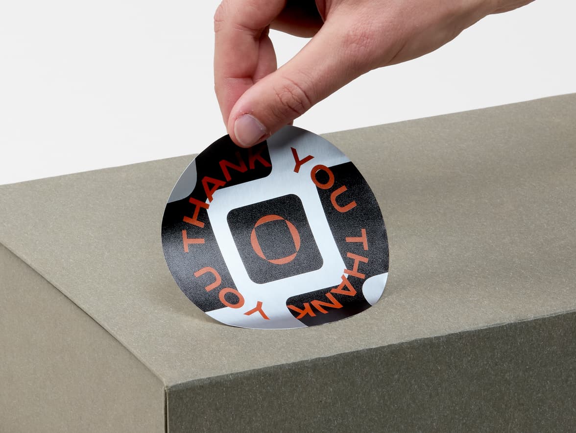 A hand placing a large round silver sticker on a box.