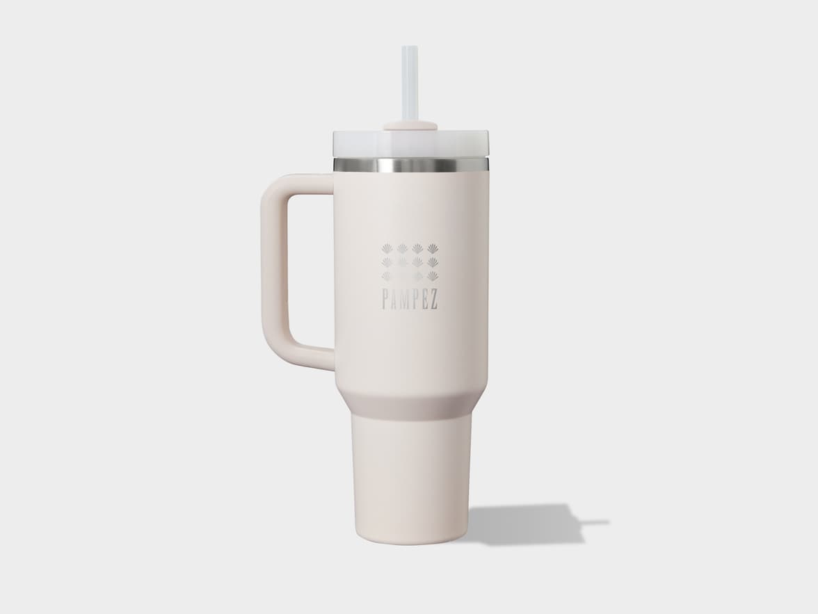 Light cream-colored tumbler with a handle and straw, featuring a subtle "PAMPEZ" logo and palm frond design, casting a shadow on a light grey background.