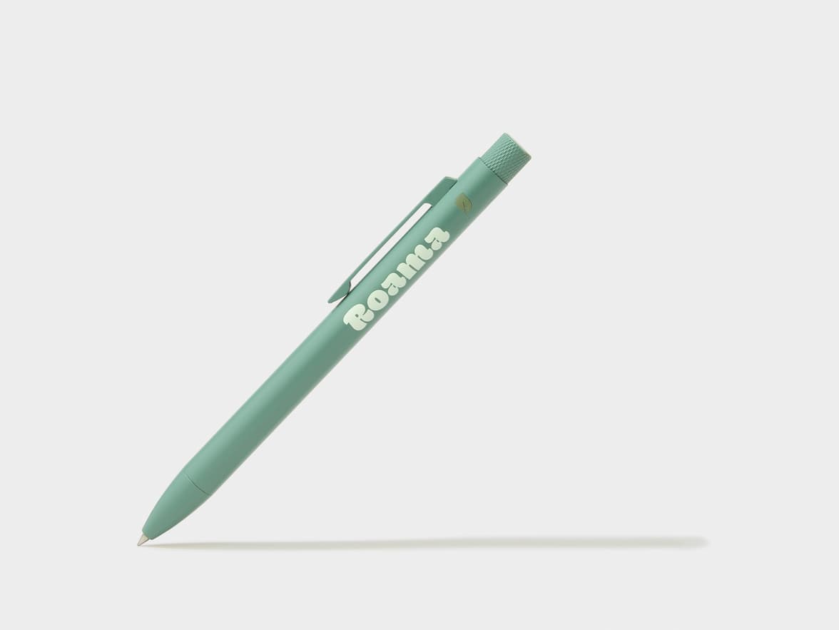 A green pen with "Roama" and a leaf icon printed on its side, casting a shadow on a light background.