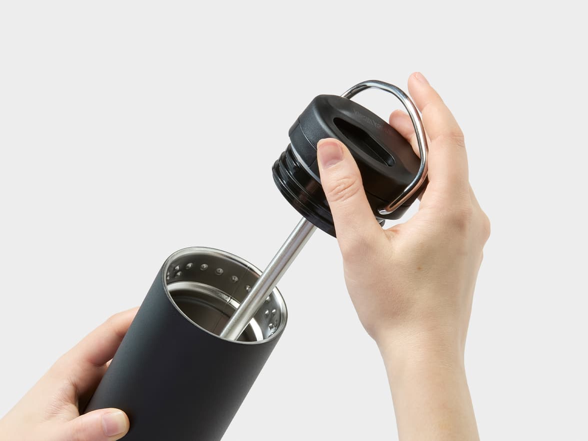 Black Klean Kanteen bottle with lid and straw being held by hands.