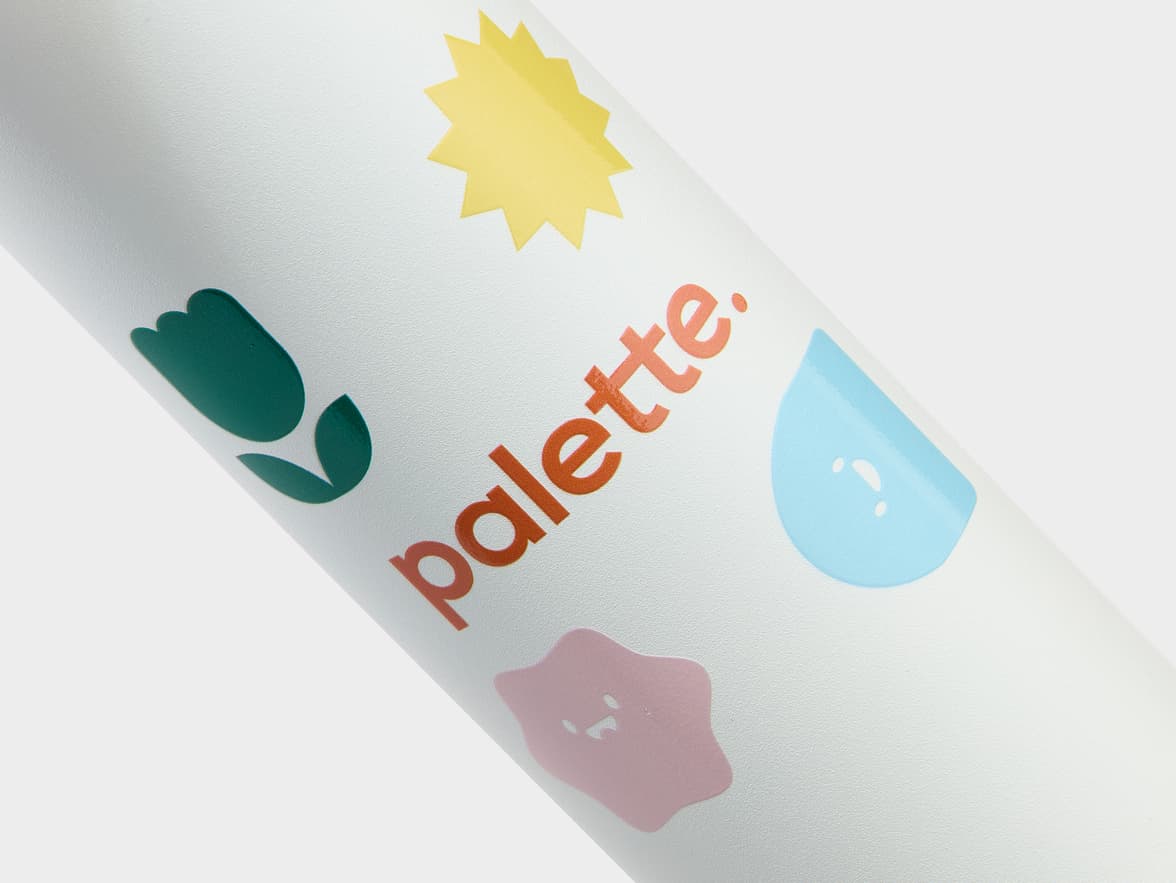 Close-up of a white bottle branded with 'palette.' and colorful abstract shapes including a green tulip, a yellow starburst, a blue teardrop, and a pink blob.