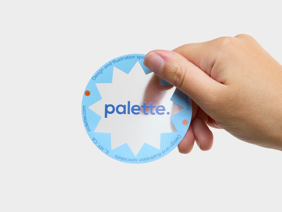 A hand holding a customized clear round sticker with a light blue jagged outline and the word 'palette' printed on it.