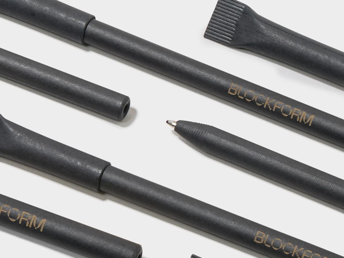 Close-up of dark grey BLOCKFORM writing tools, including pens and a brush, on a white surface.