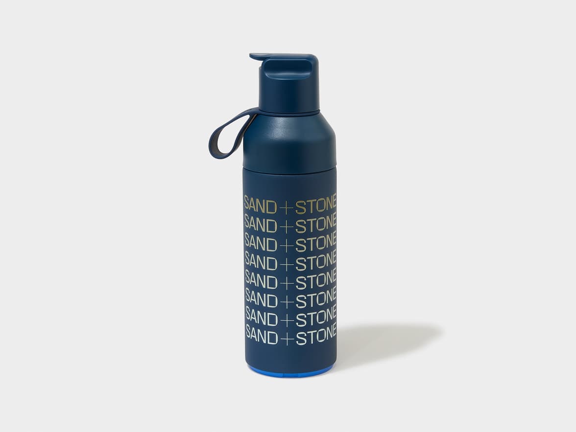 Dark blue water bottle with SAND + STONE branding repeated vertically.