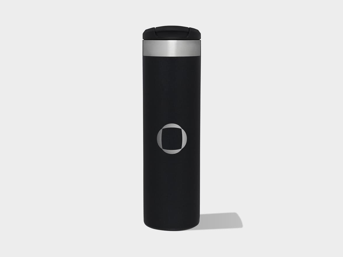 A black travel bottle with a silver band, black lid, and a silver circular logo with a square cutout.