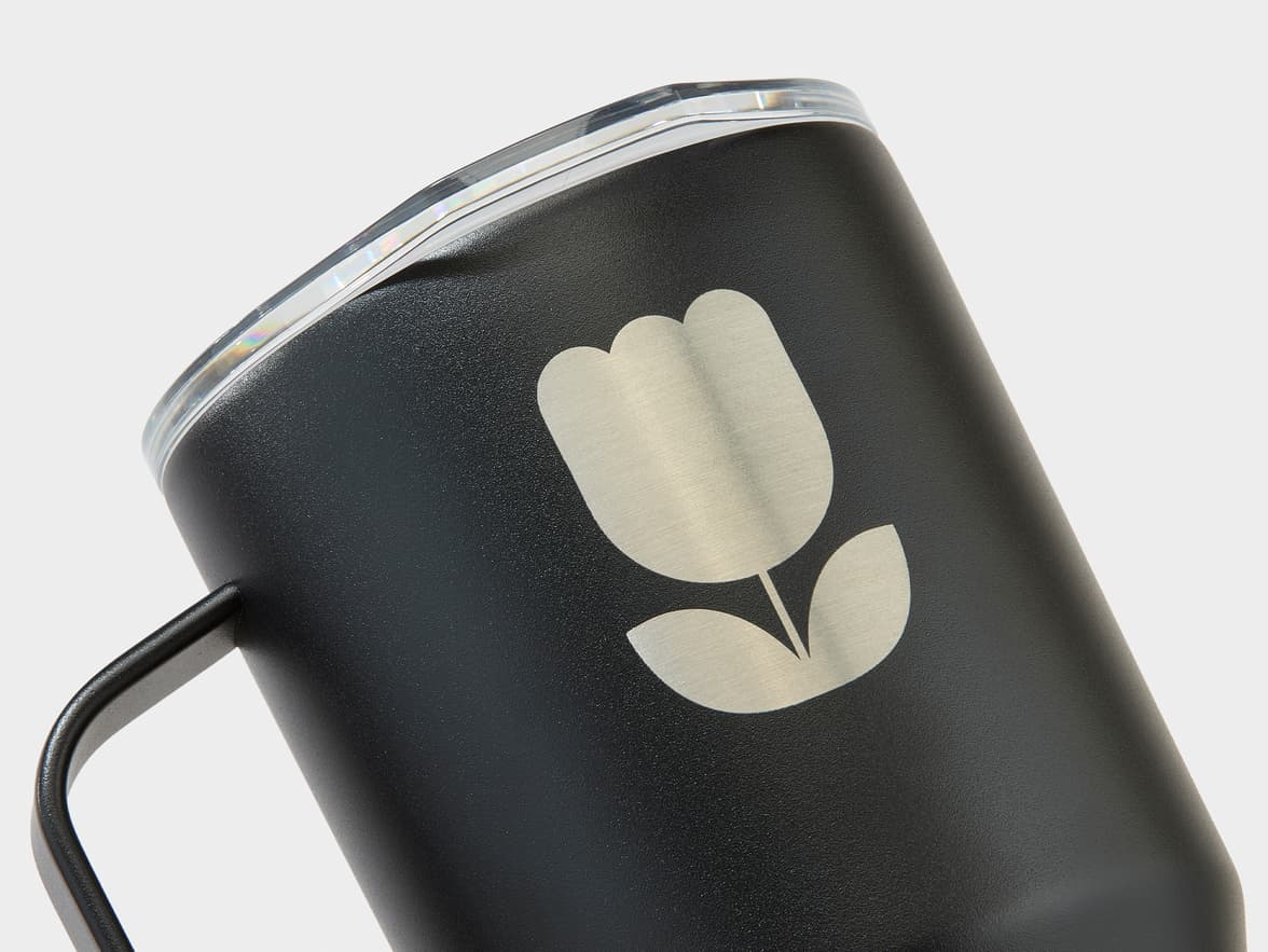 A black mug with a clear lid features a silver, brushed metal tulip logo on its side.