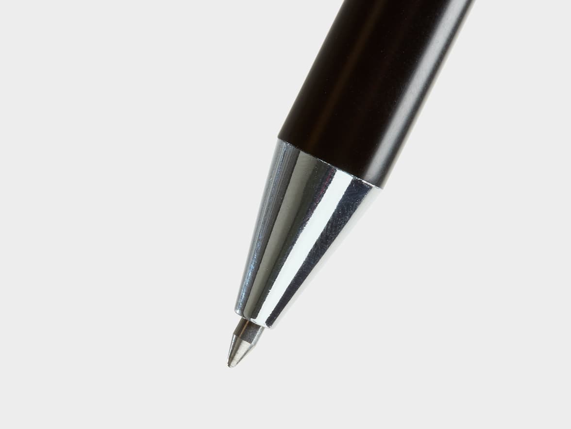 A close-up of the silver metallic tip of a dark-colored ballpoint pen.