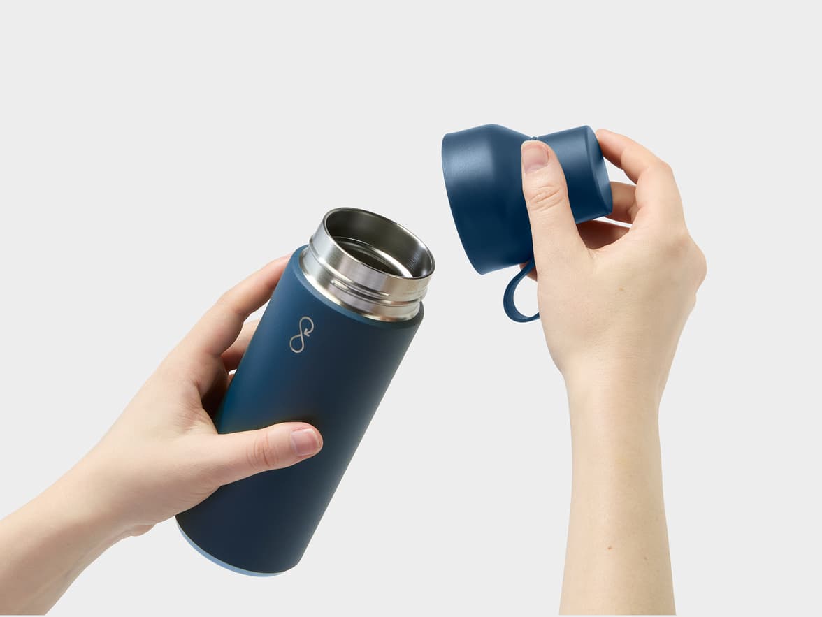 A person holds a dark blue insulated bottle with an infinity loop logo, its lid removed.