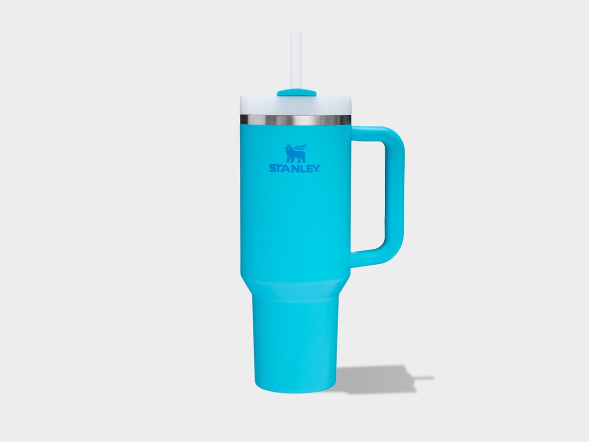 A light blue Stanley tumbler with a white lid, straw, and handle, featuring the Stanley logo, on a light background.