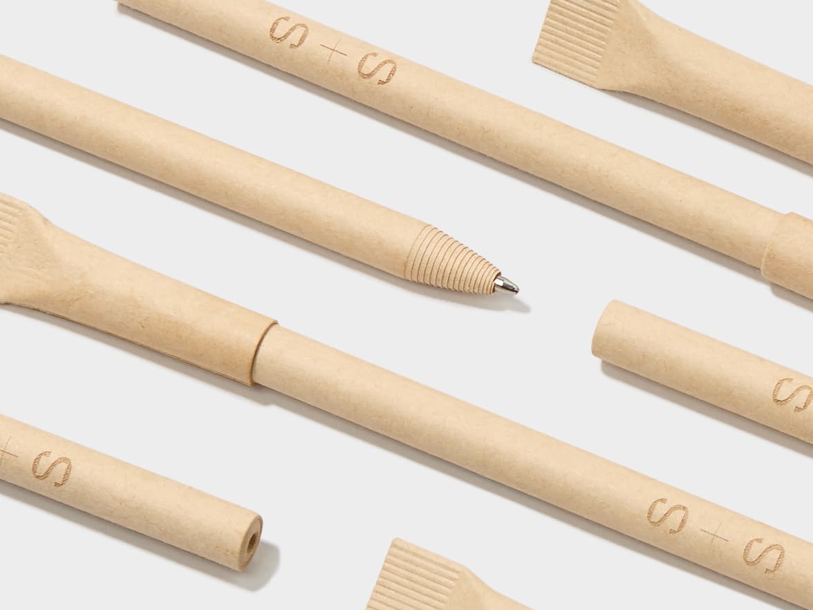 Several light brown pens, some featuring the "S + S" logo, are arranged on a white surface.