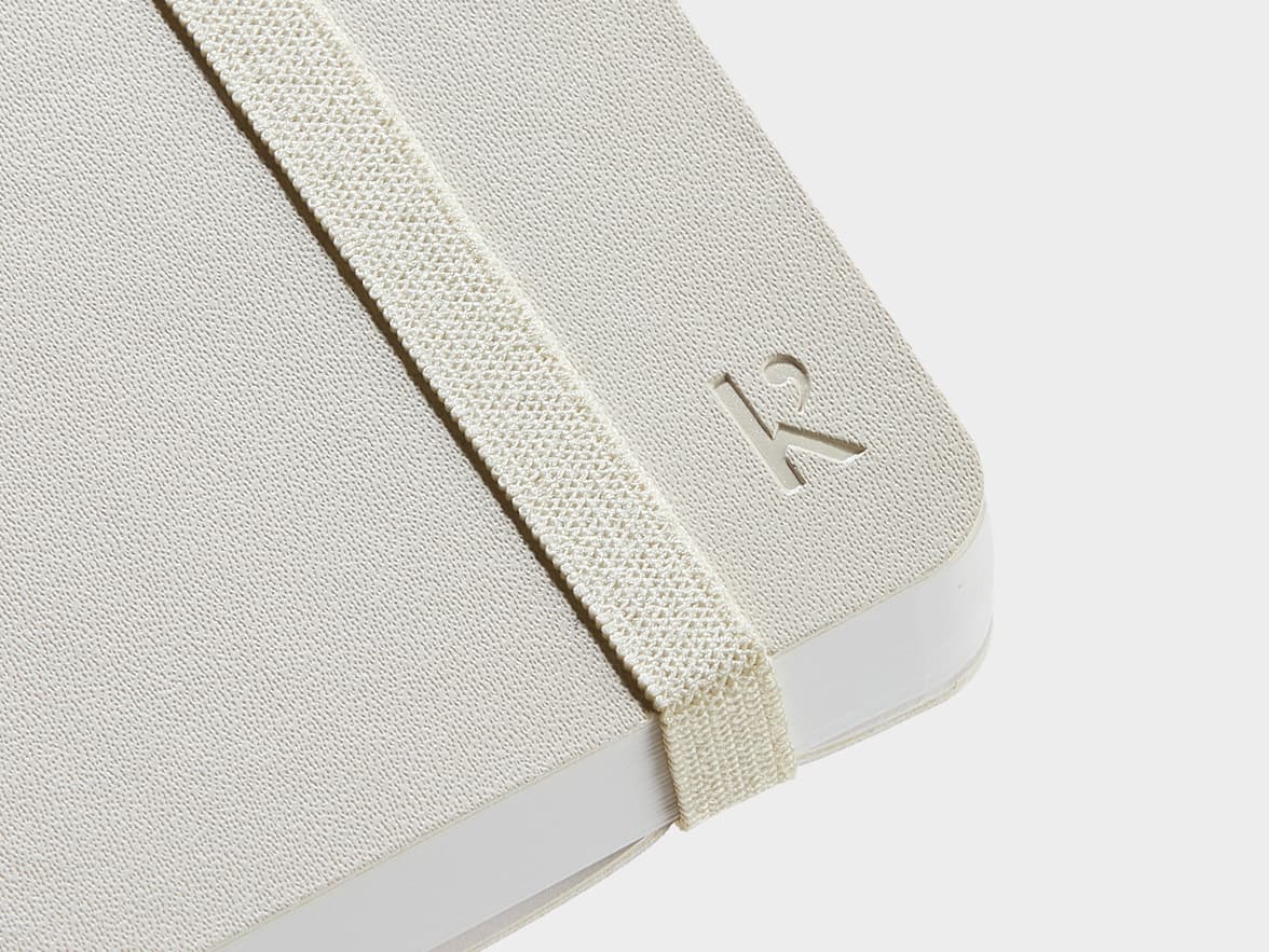 Close up shot of the corner of the cover of the Beige Karst Stone Paper Pro Series Softcover Notebook with Karst branding and strap
