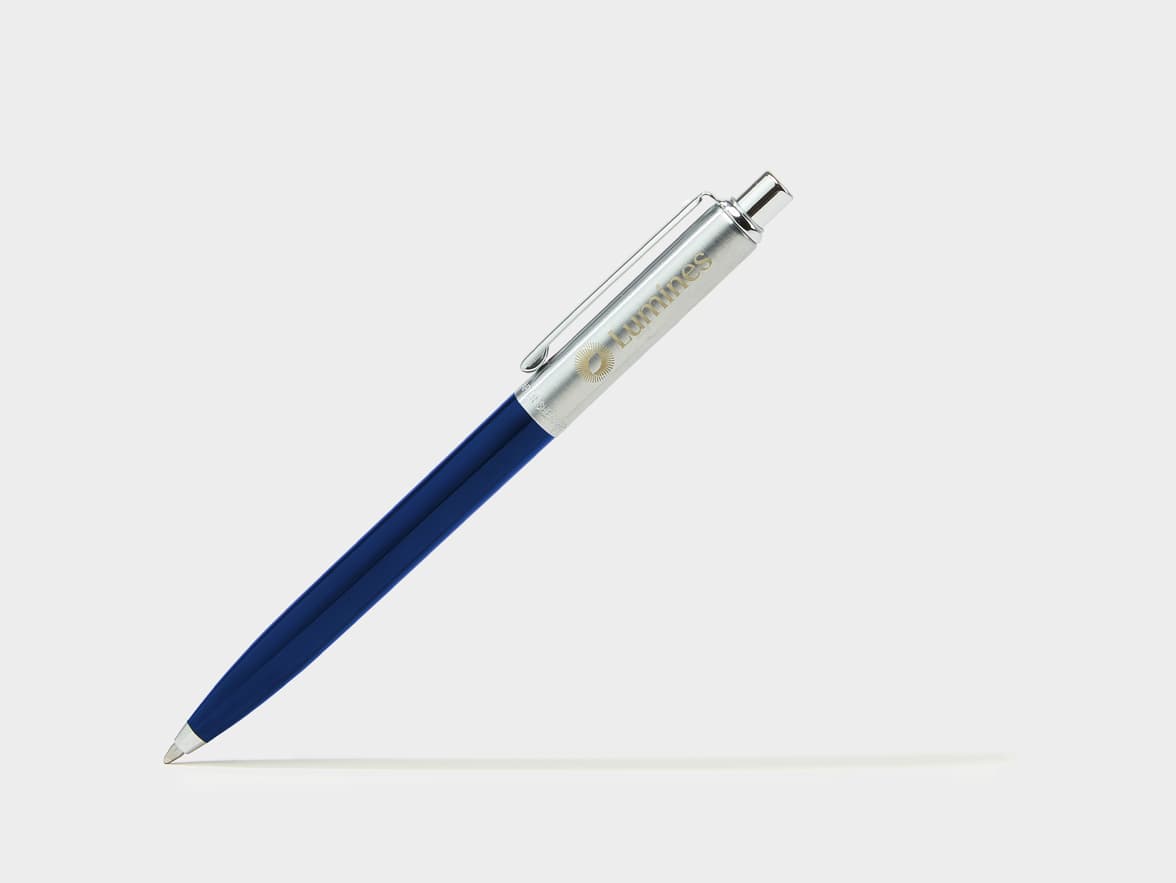 A blue and silver ballpoint pen with the "Lumines" brand and a sun logo on its barrel, resting at an angle.