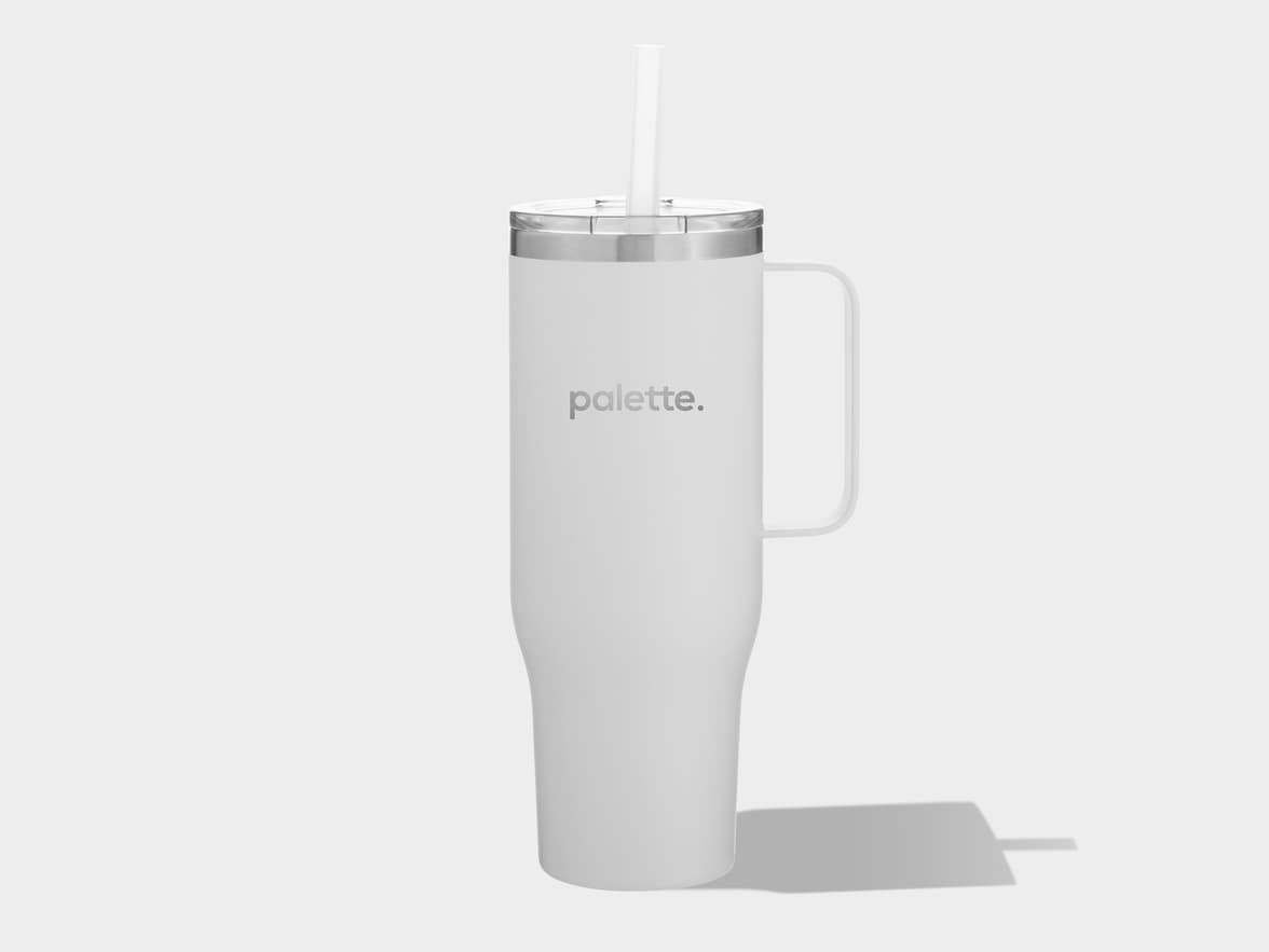 A tall, light grey travel tumbler with a matching handle on the right side. It features a silver rim just below a clear lid, from which a white straw extends upwards. The word 'palette.' is printed in dark grey lowercase letters on the front of the tumbler. The tumbler casts a subtle shadow to its right on a plain, light grey background.