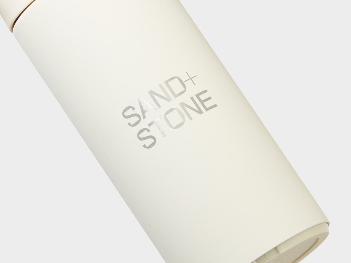 A cream-colored bottle with "SAND + STONE" branding.