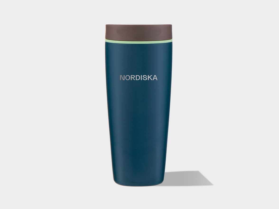 A tall, dark teal reusable bottle with a brown lid and a thin light green band below the lid, casting a shadow to its right on a light grey background. The word "NORDISKA" is written vertically in light grey letters on the side of the bottle.
