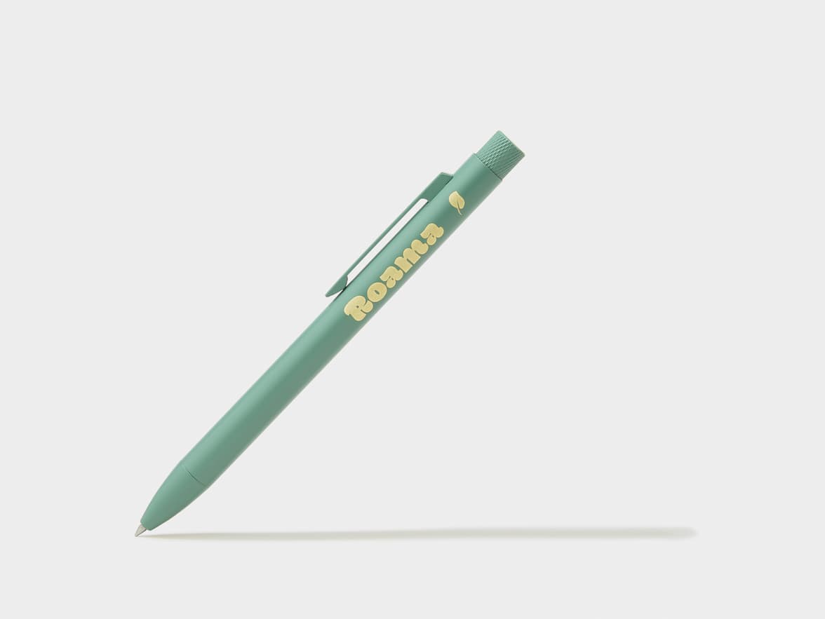A mint green pen with "Roama" and a leaf logo printed in gold, resting at an angle on a white surface.