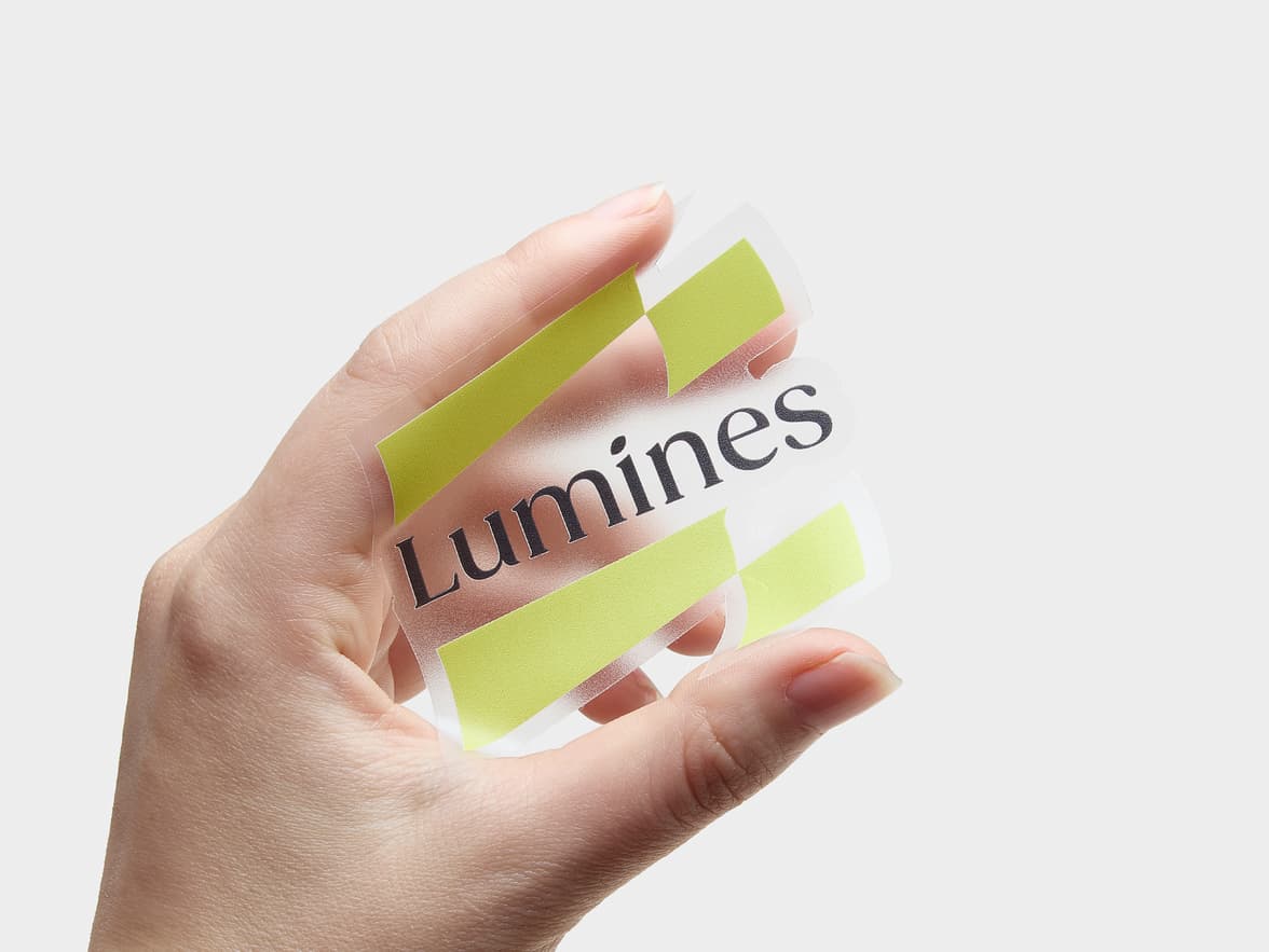 A hand holding a customized clear die cut sticker with the colour lime green and word 'Lumines' printed on it.