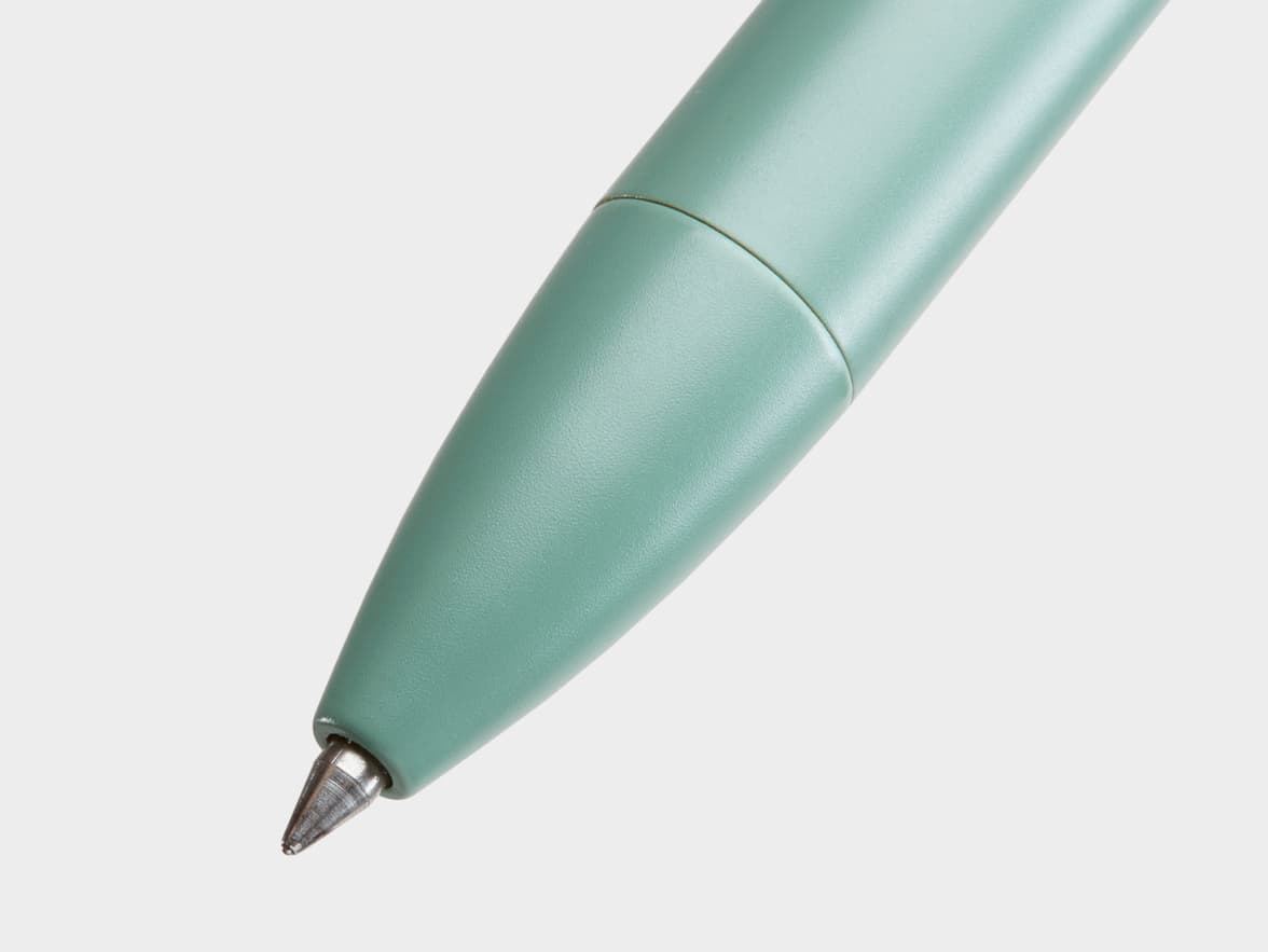 A close-up of the tip of a teal pen with a silver writing point, angled against a light gray background.