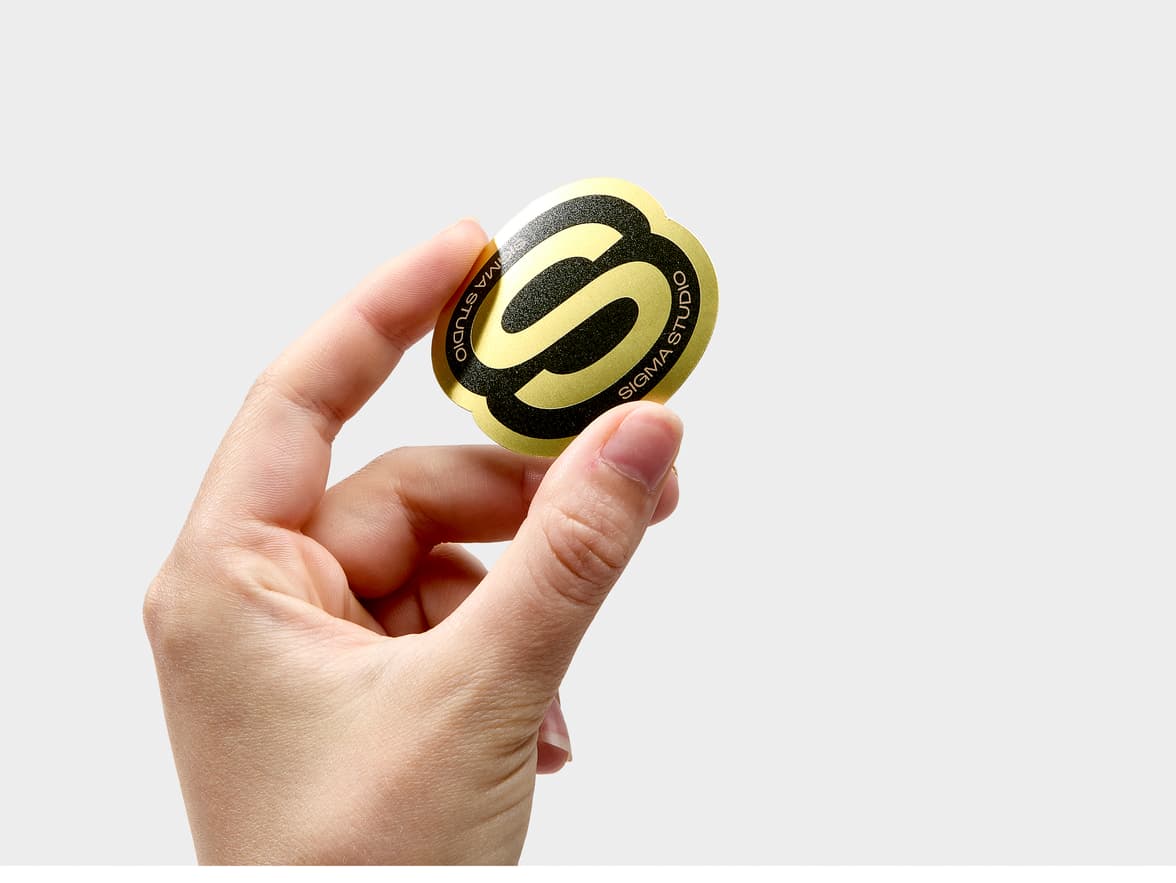 A hand holding a customized gold metallic sticker in the shape of a bold S.