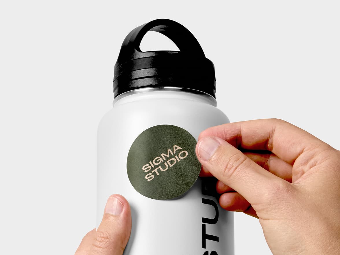 A hand placing a dark green customized round coated sticker onto a water bottle.