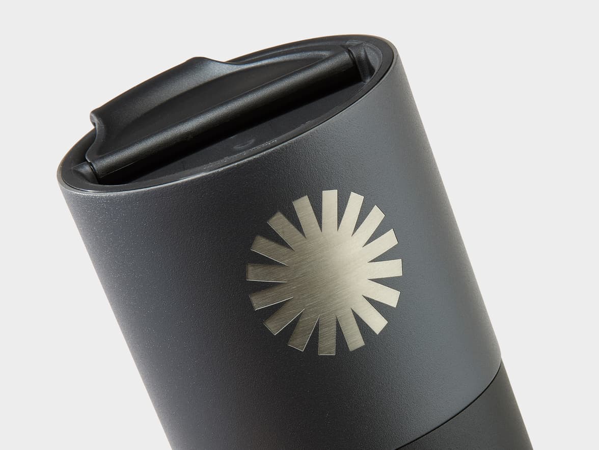 Dark gray tumbler with a brushed silver 12-ray sunburst emblem.