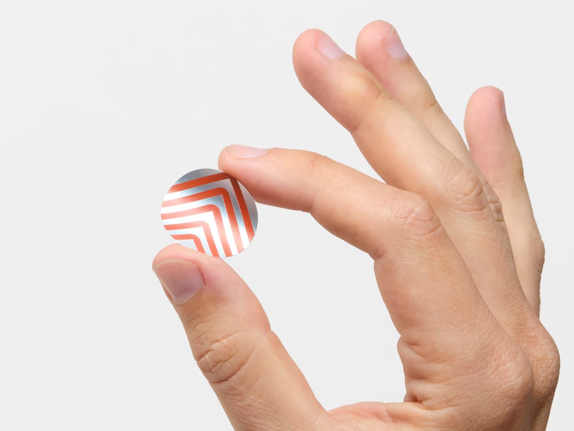 A hand holding a round silver metallic sticker with orange customization.