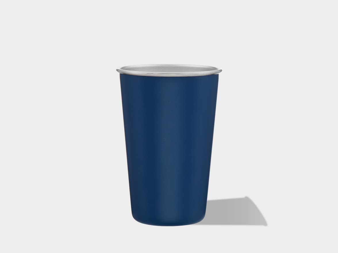 A dark blue metal tumbler cup with a silver rim sits centered on a clean white surface, casting a soft shadow to its right.