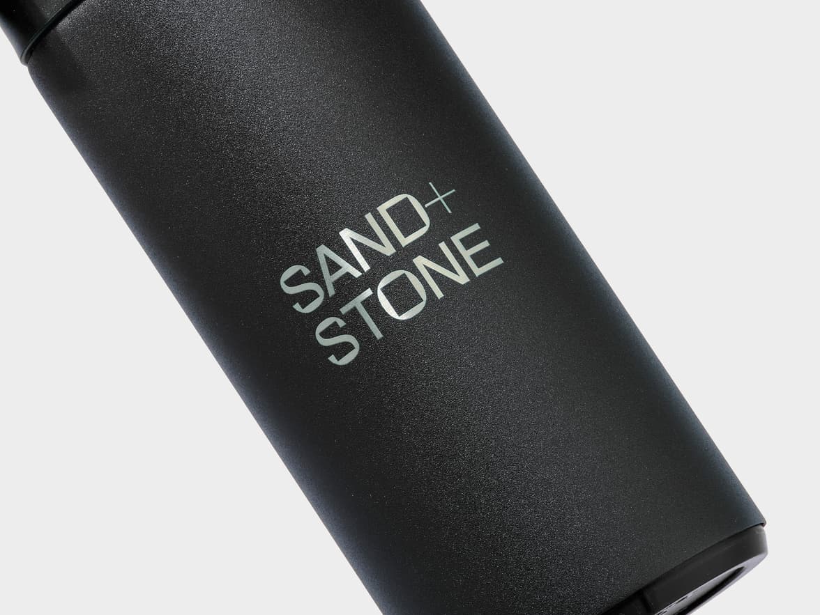 Black textured bottle with "SAND+ STONE" logo.
